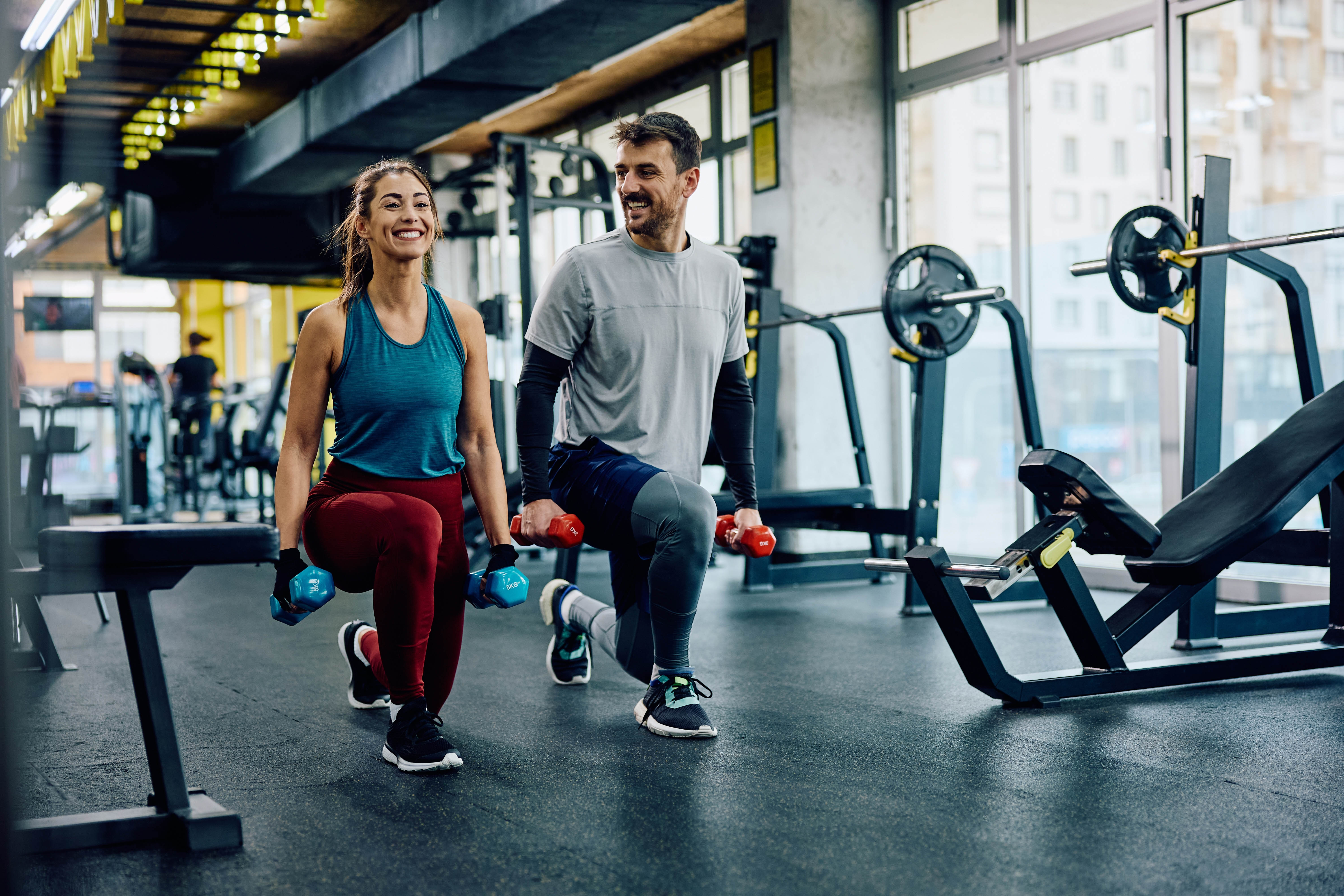 Young couple working out together in the gym, smiling at each other as they complete a set of lunges